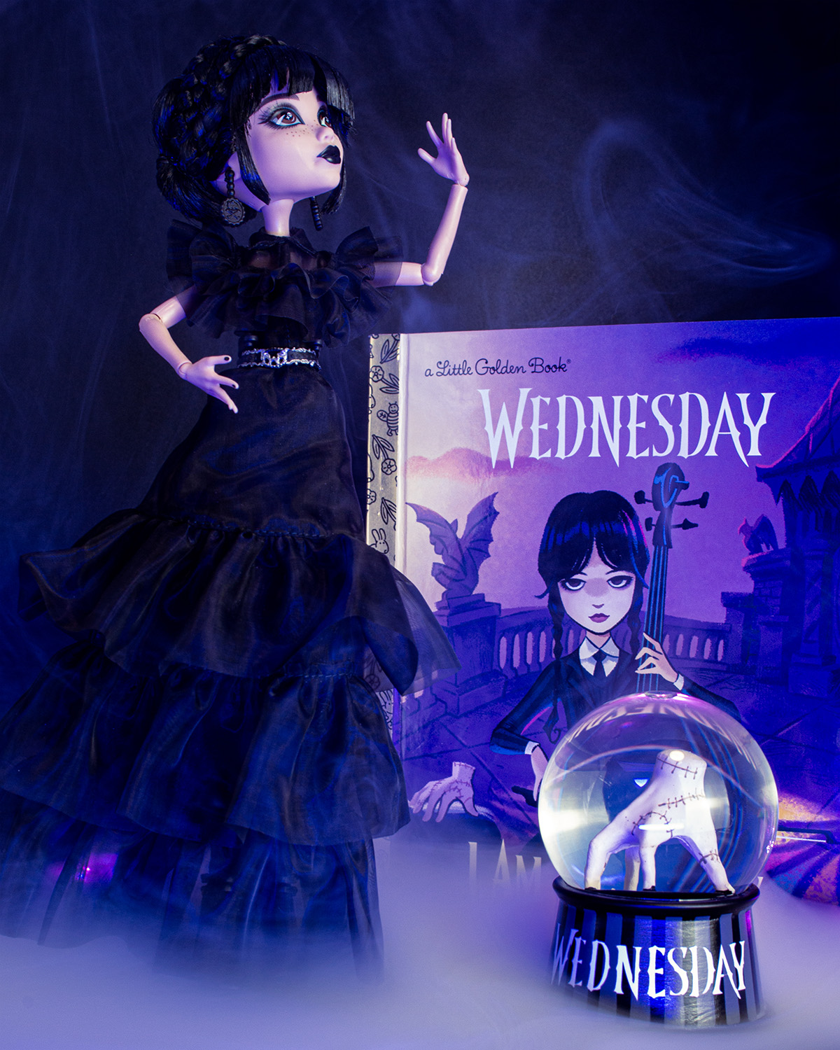 Wednesday product display featuring Monster High doll, Little Golden Book, and snow globe with Thing inside